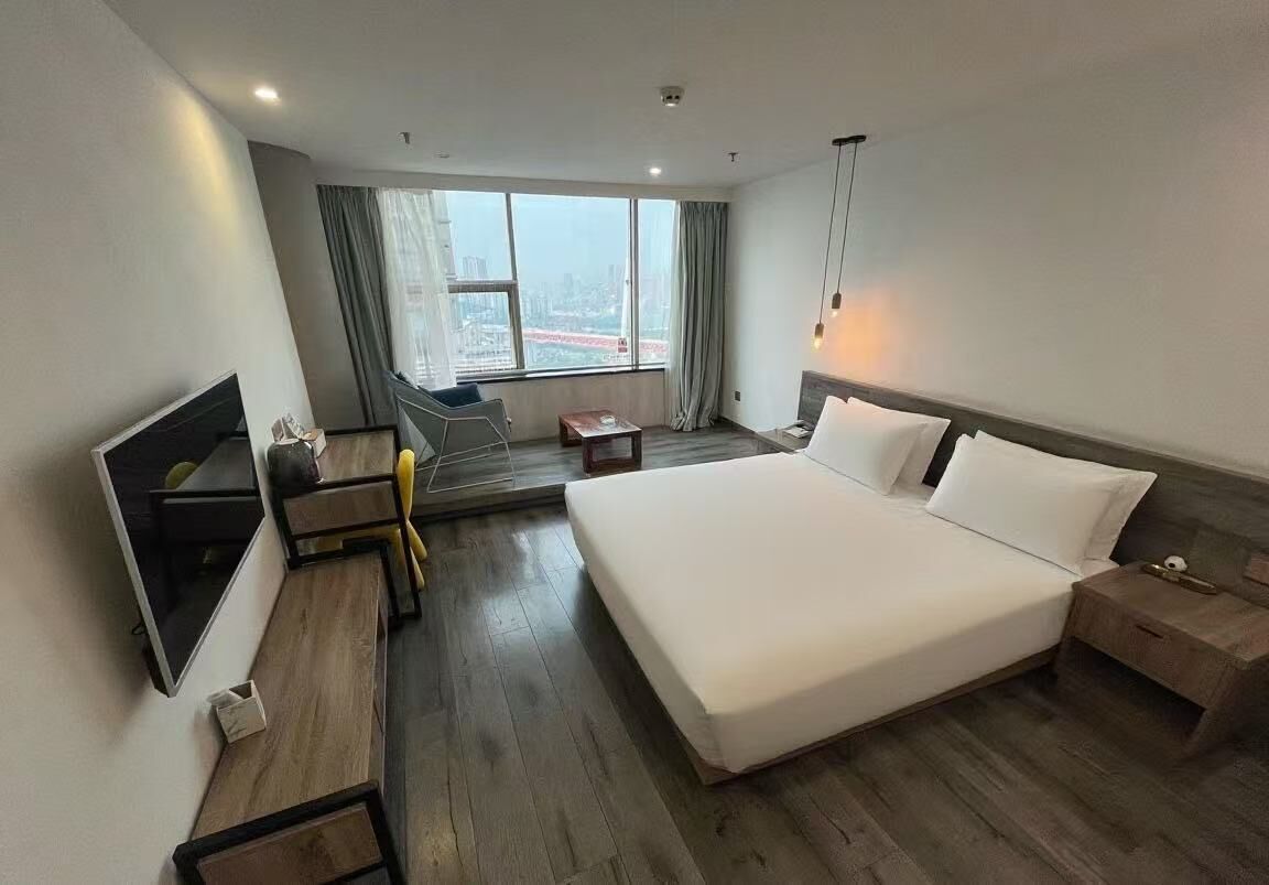 Habitació d'hotel moderna amb un llit gran, escriptori, cadira, televisió i vista a la ciutat per la finestra.