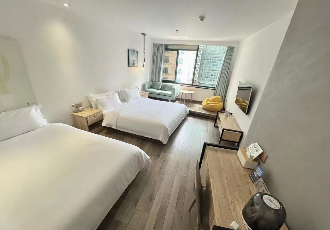 A hotel room with two beds, a sofa, a small table, and a window with curtains.