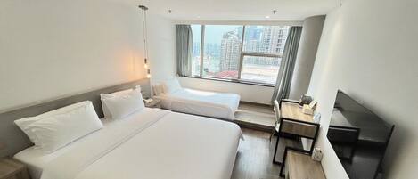 Habitación de hotel con dos camas, un escritorio, un televisor y una ventana con vistas a la ciudad.