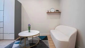 A modern room with a white sofa, a round table with a vase, a wardrobe, and a shelf with a clock and decorative items.