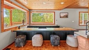 A modern kitchen with large windows, a wooden ceiling, and three stools.