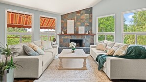 A living room with a fireplace, two sofas, a coffee table, and large windows with curtains.