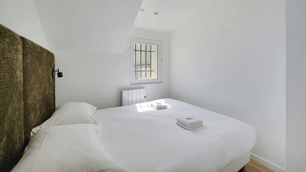 Une chambre avec un lit simple, une fenêtre avec des barreaux et un radiateur.