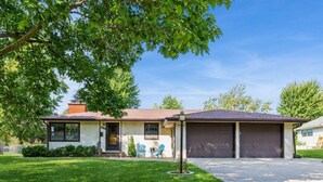 Ein eingeschossiges Haus mit Garage, einer Veranda mit zwei Stühlen und einem gepflegten Rasen.