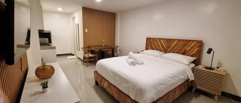 Ein modernes Hotelzimmer mit einem hölzernen Bett, einem Schreibtisch, einem Sessel, einem kleinen Tisch mit einer Vase und einem Fernseher.