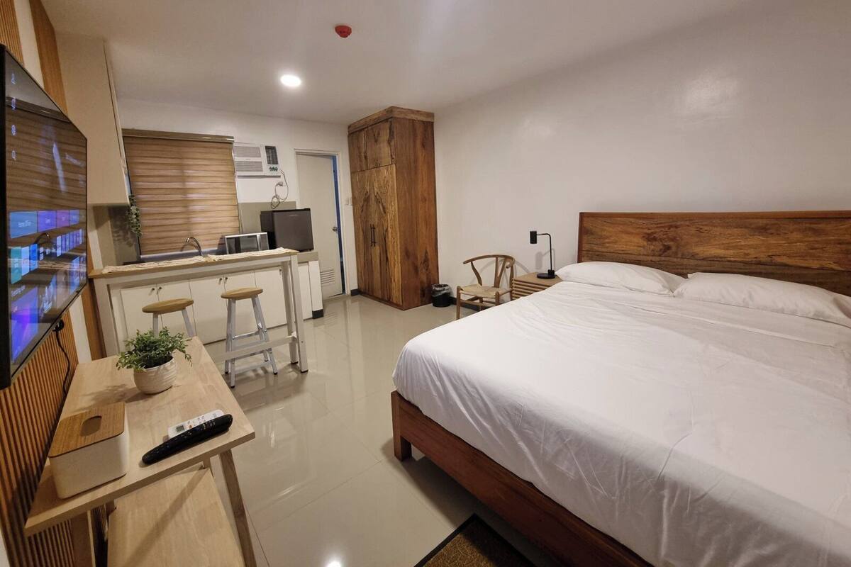 Ein modernes Hotelzimmer mit einem Bett, einem Schreibtisch mit Computer, einem Sessel und einem Fernseher.