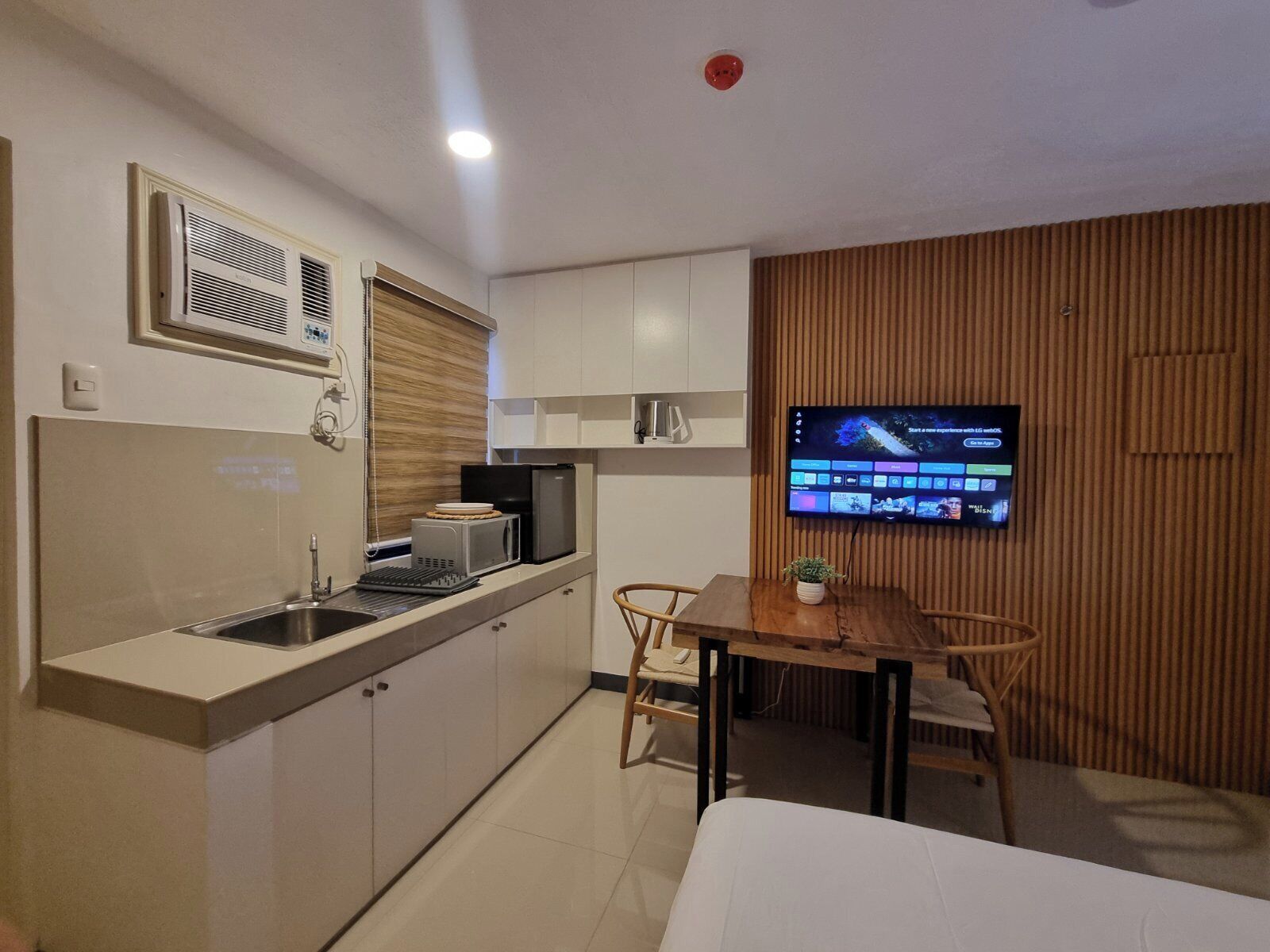 Una cocina compacta equipada con microondas, tostadora y pileta, un comedor con mesa y sillas, y un televisor de pantalla plana montado en la pared.