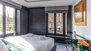 A hotel room with a large bed, a window with a view of buildings, a painting on the wall, and a vase with flowers on a side table. - Modern Apartment - 1br/4p - Pereire (Paris)