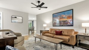A modern living room with a sofa, coffee table, and a painting of a cityscape. - Howdy: King Beds/2 Miles to Campus (4BR/2Ba) (Bryan)