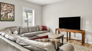 A living room with a leather sofa, a wooden coffee table, and a flat-screen TV. - Howdy: King Beds/2 Miles to Campus (4BR/2Ba) (Bryan)