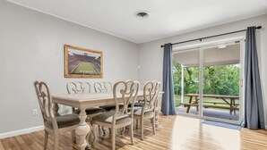 A dining area with a wooden table and chairs, a framed picture on the wall, and a view of an outdoor patio with a picnic table. - Howdy: King Beds/2 Miles to Campus (4BR/2Ba) (Bryan)