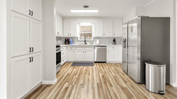 A modern kitchen with white cabinets, a stainless steel refrigerator, and a wooden floor. - Howdy: King Beds/2 Miles to Campus (4BR/2Ba) (Bryan)