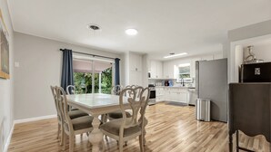 A modern kitchen with white cabinets, a stainless steel refrigerator, and a dining area with a wooden table and chairs. - Howdy: King Beds/2 Miles to Campus (4BR/2Ba) (Bryan)