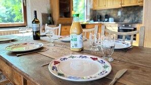 A wooden dining table set with plates, glasses, and a bottle of wine in a kitchen with wooden cabinets and a window. - An oasis of tranquility in the heart of nature (Rendeux)