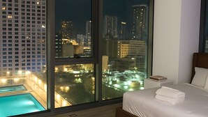 A modern bedroom with a large window overlooking a cityscape at night.