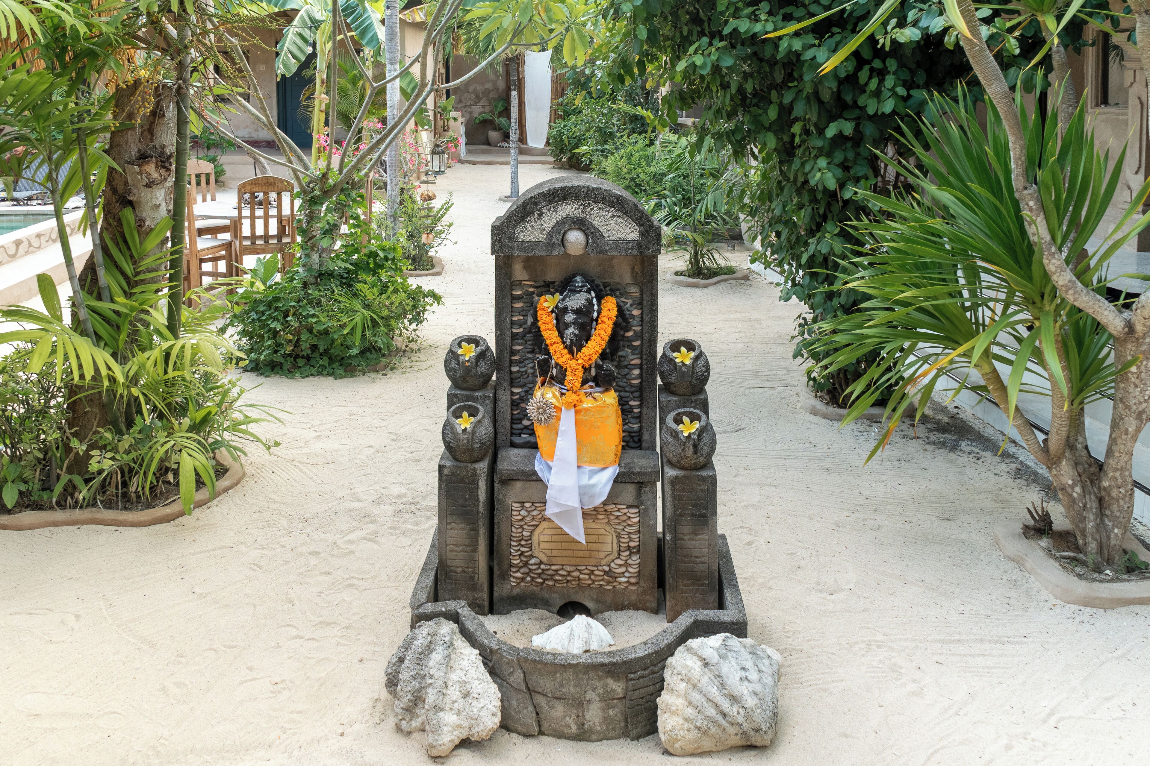 A stone structure with a carved seat, surrounded by sand and greenery.