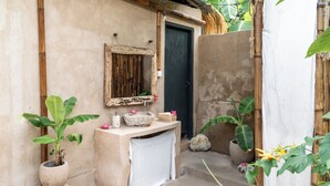 A small, rustic bathroom with a stone sink, a mirror, and a door. There are potted plants around the sink and a small step leading to the door. - The House of The Rising Tide Boutique Hotel (Lembongan Island)
