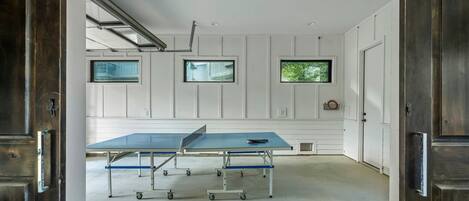 Una habitación con mesa de ping pong, paredes blancas y tres ventanas.