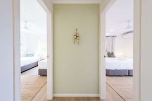 A hallway leading to two bedrooms with a ceiling fan, a light fixture, and a wall-mounted towel rack. - Crest on Convent - Oceanstays - Steps to Cafes, Beaches & Town (Yamba)