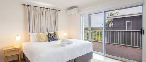A bedroom with a large bed, a nightstand with a lamp, a ceiling fan, and a sliding glass door leading to a balcony.
