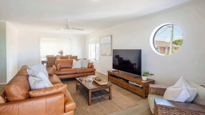 Ein modernes Wohnzimmer mit einem braunen Ledersofa, einem Holztisch, einem Fernseher auf einem Holzständer und einem runden Fenster mit Blick nach draußen.