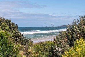 A beach with waves, a clear sky, and some vegetation in the foreground. - Crest on Convent - Oceanstays - Steps to Cafes, Beaches & Town (Yamba)