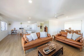 A spacious living area with two leather sofas, a coffee table, and a dining area with wicker furniture. - Crest on Convent - Oceanstays - Steps to Cafes, Beaches & Town (Yamba)