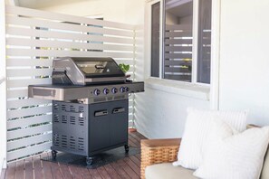 A portable grill on a deck with a white fence and a window in the background. - Crest on Convent - Oceanstays - Steps to Cafes, Beaches & Town (Yamba)