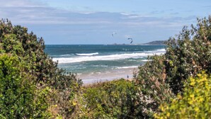 Ein Strand mit Wellen, blauem Himmel und etwas Vegetation im Vordergrund.