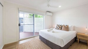 Ein Schlafzimmer mit einem großen Bett, einem Nachttisch aus Holz, einer Stehlampe und einer Glastür zum Balkon.