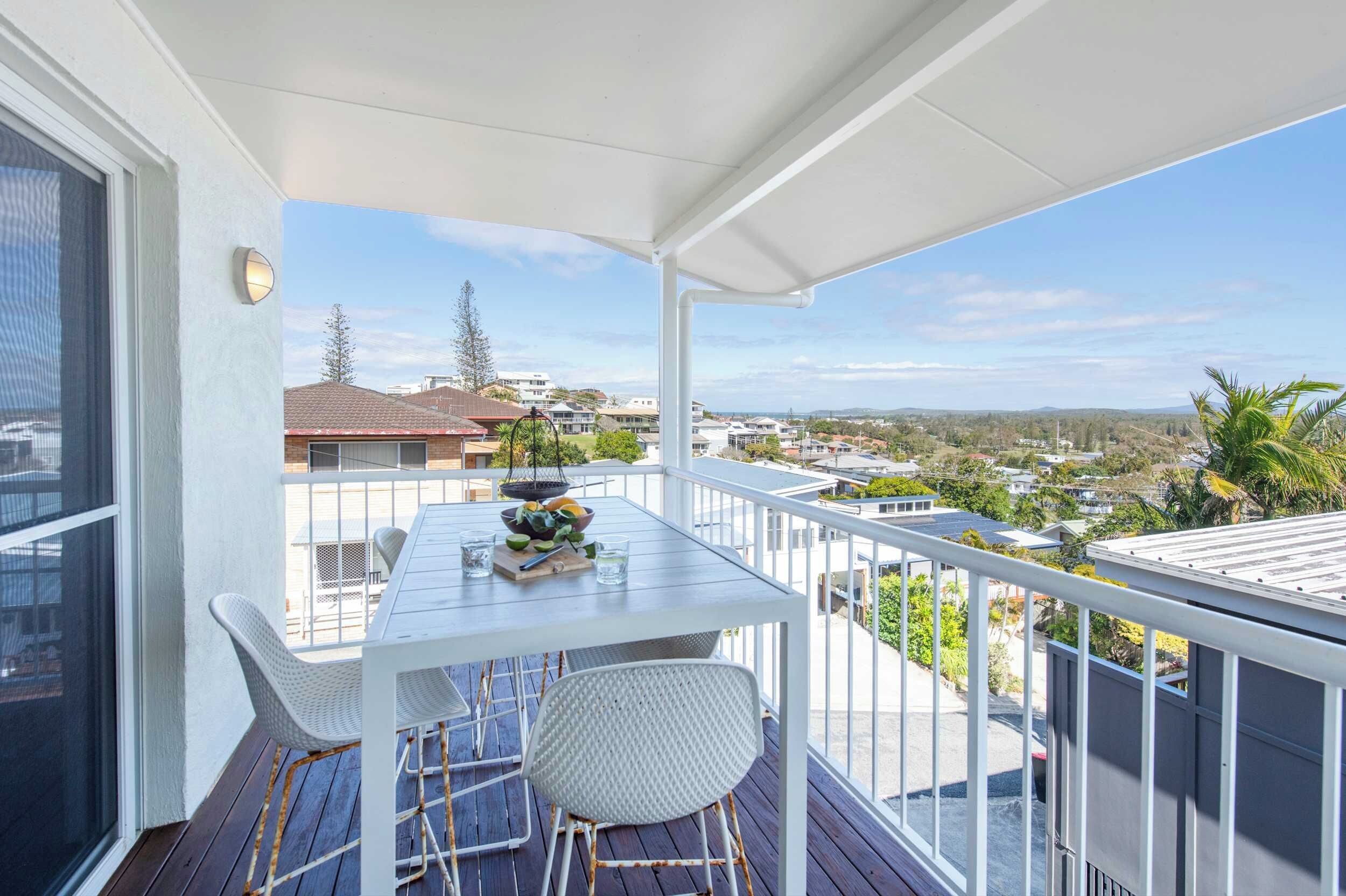 Ein Balkon mit weißem Tisch und Stühlen, einer Obstschale und Blick auf eine Wohngegend.