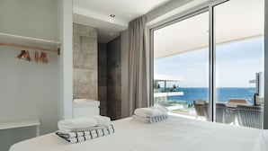 Une chambre d’hôtel moderne dotée d’un grand lit, d’une salle de bain avec douche et d’un balcon offrant une vue sur l’océan.