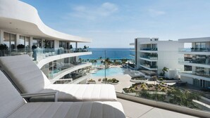 Un hôtel moderne à l’architecture extérieure incurvée, doté d’un espace piscine avec des chaises longues et offrant une vue sur l’océan.