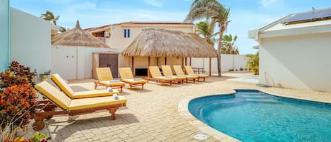 A pool area with lounge chairs and a thatched-roof structure.