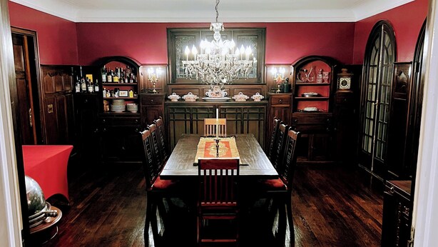 A dining room with a long wooden table, chairs, a chandelier, and wooden cabinets.