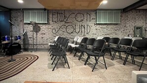 A room with a brick wall, a sign reading "EDISON SOUND", and rows of black chairs.