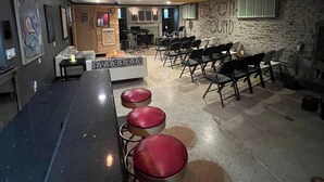 A bar area with stools and a counter, a seating area with a sofa and chairs, and a brick wall with graffiti.