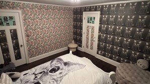 A bedroom with a bed featuring a large cat print, patterned wallpaper, and a ceiling light fixture.
