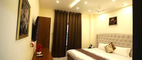 A hotel room with a bed, a bedside table with a vase, a framed picture on the wall, and a window with curtains.