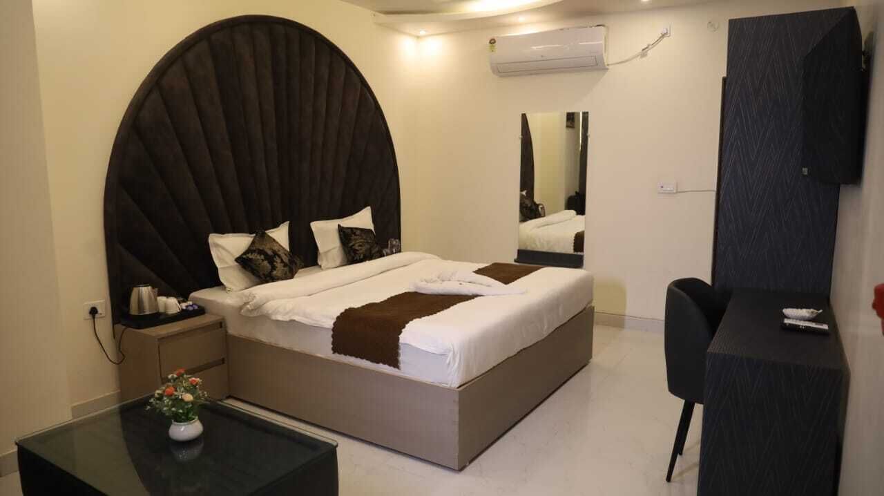 A modern hotel room with a large bed, a desk, and a chair. There is a mirror on the wall and an air conditioning unit.
