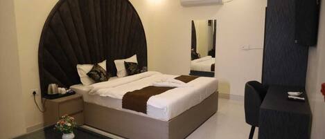A modern hotel room with a large bed, a desk, and a chair. There is a mirror on the wall and an air conditioning unit.