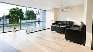 A modern interior with a glass partition, a black leather sofa, and a potted plant. - Hotel R Raghavam (Ayodhya)