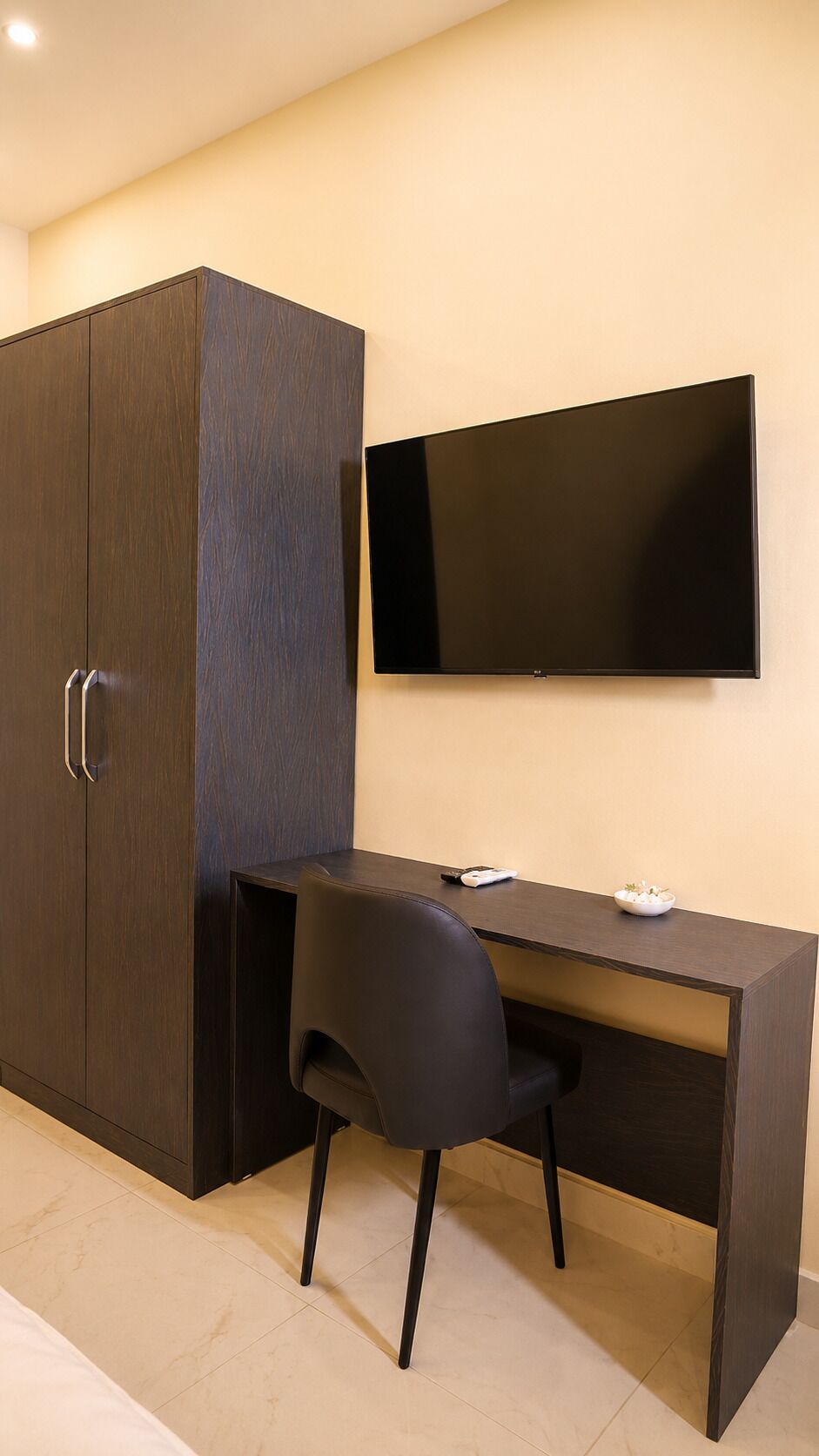 Una habitación moderna con un armario de madera oscura, un escritorio con silla y un televisor de pantalla plana montado.