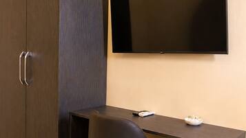 Een moderne kamer met een donkere houten garderobe, een bureau met stoel, en een wandgemonteerde flatscreen-televisie.