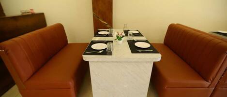 A dining area with a marble table set for two, flanked by brown leather sofas.