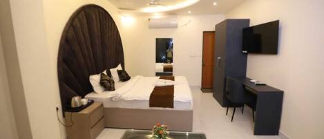 A modern bedroom with a large bed, a desk, and a TV.