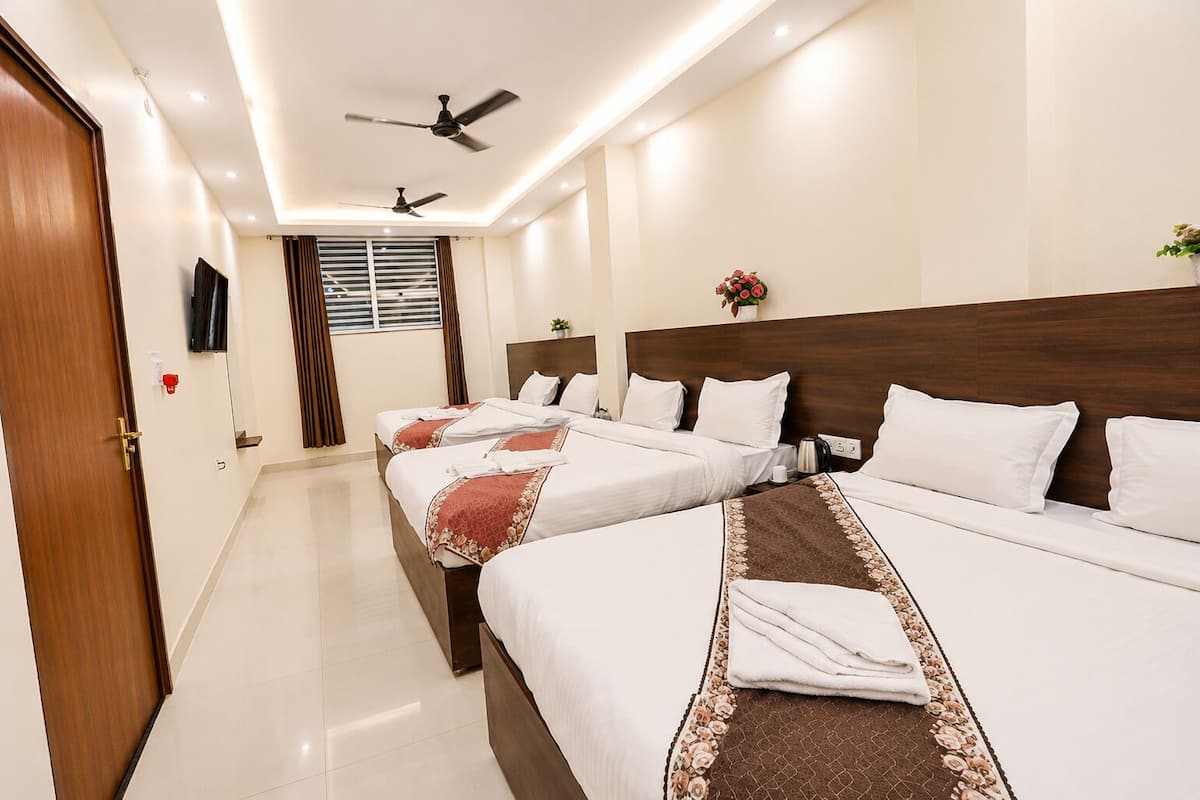 Quarto de hotel com três camas, ventilador de teto, televisão e janela com cortinas.