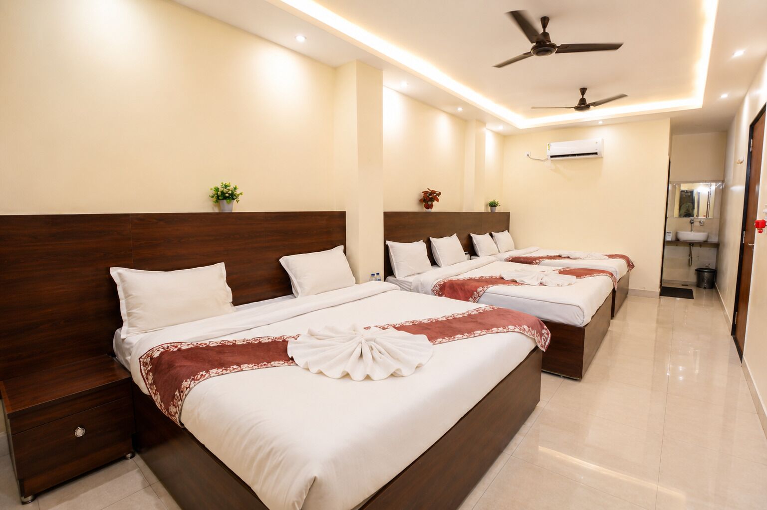 Une chambre d’hôtel avec quatre lits, un ventilateur de plafond, un climatiseur mural et une petite plante.