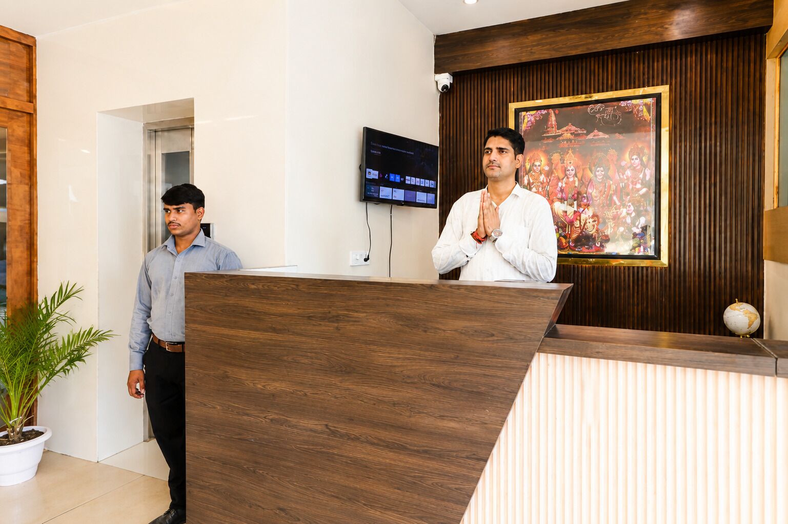 A reception desk with a wooden finish, a television mounted on the wall, and a framed picture above the desk.