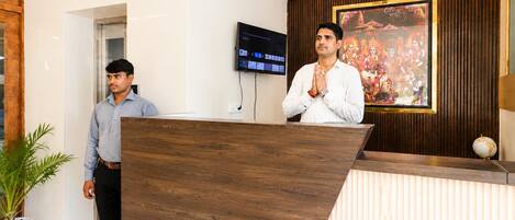 A reception desk with a wooden finish, a television mounted on the wall, and a framed picture above the desk.